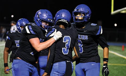 Two men wearing football uniforms are hugging each other on a field. AI generated content