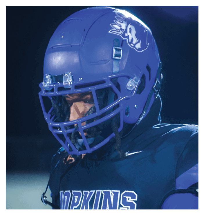 A football game is in progress with players on the field. One player is throwing a football while another player is trying to catch it. The players are wearing uniforms and are actively engaged in the game. AI generated content