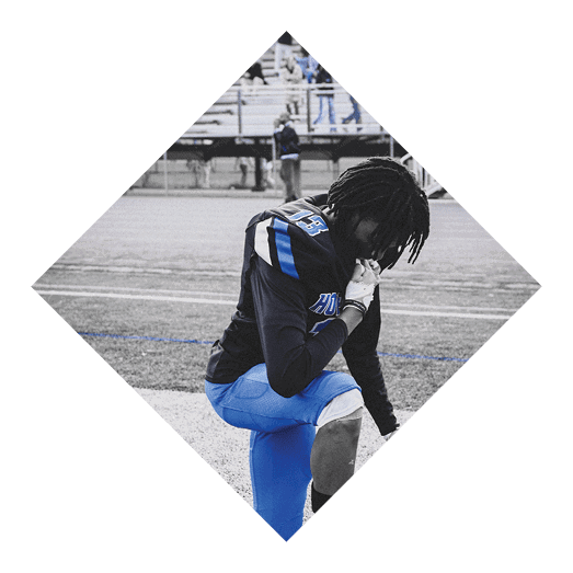 A football player wearing a black jersey with the number 10 sits on the ground with a football helmet on the ground next to him. AI generated content