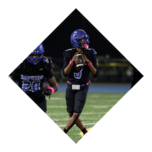 A football player wearing a black jersey with the number 10 sits on the ground with a football helmet on the ground next to him. AI generated content