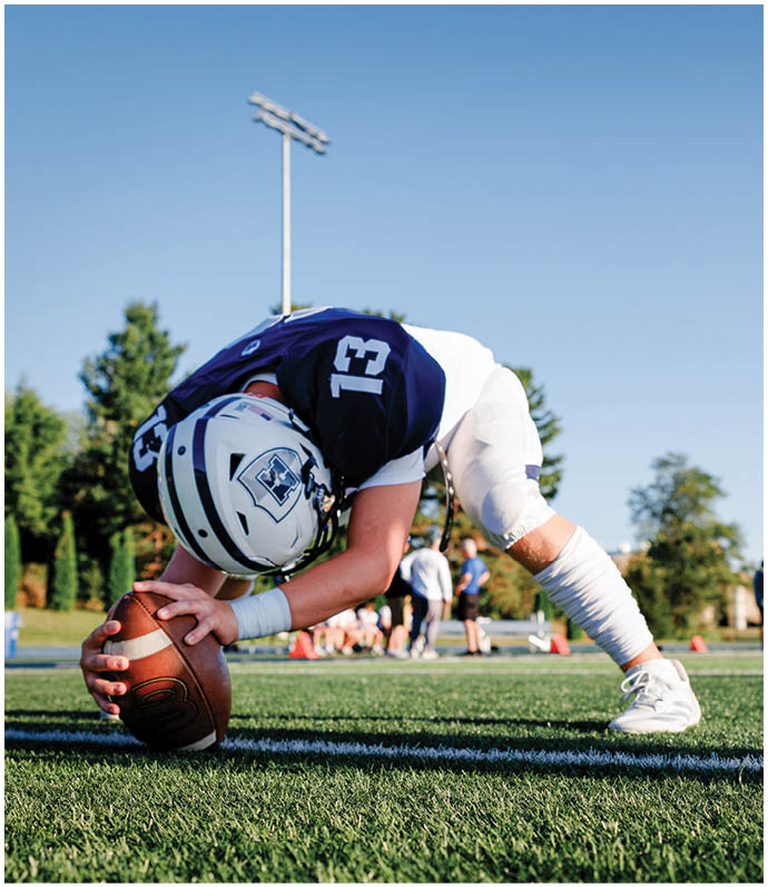 Three football players in blue and white uniforms running on a field. Description generated by AI