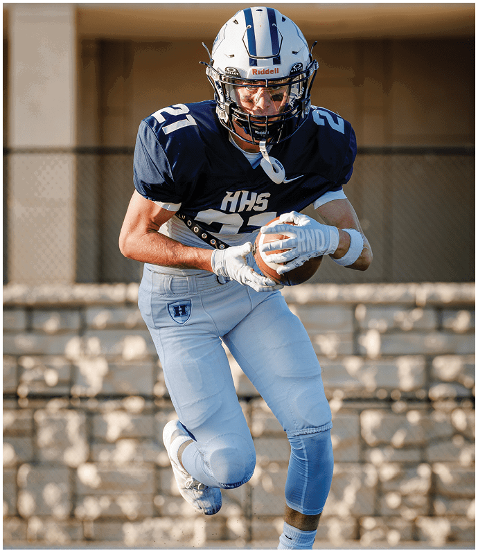 Three football players in blue and white uniforms running on a field. Description generated by AI