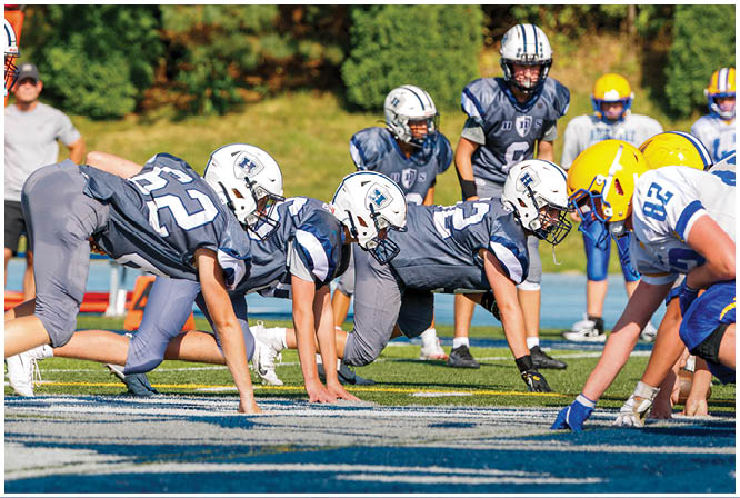 Three football players in blue and white uniforms running on a field. Description generated by AI