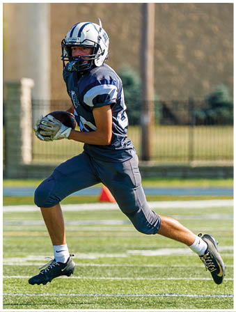 Three football players in blue and white uniforms running on a field. Description generated by AI
