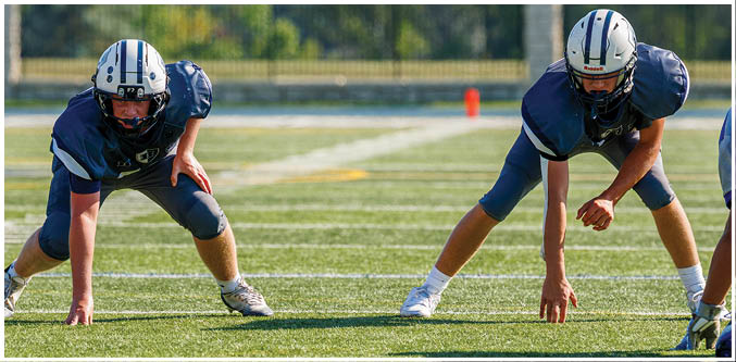 Three football players in blue and white uniforms running on a field. Description generated by AI