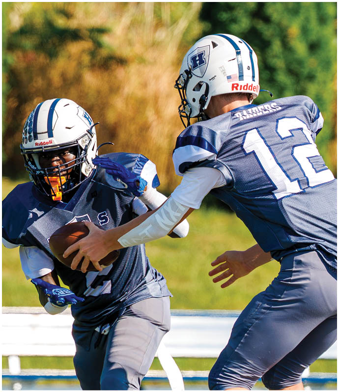 Three football players in blue and white uniforms running on a field. Description generated by AI