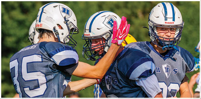Three football players in blue and white uniforms running on a field. Description generated by AI
