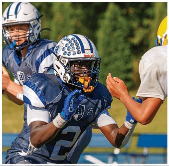 Three football players in blue and white uniforms running on a field. Description generated by AI