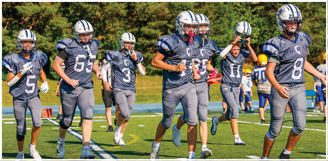 Three football players in blue and white uniforms running on a field. Description generated by AI