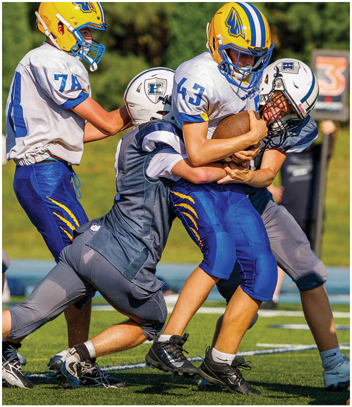 Three football players in blue and white uniforms running on a field. Description generated by AI