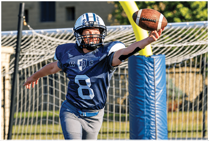 Three football players in blue and white uniforms running on a field. Description generated by AI