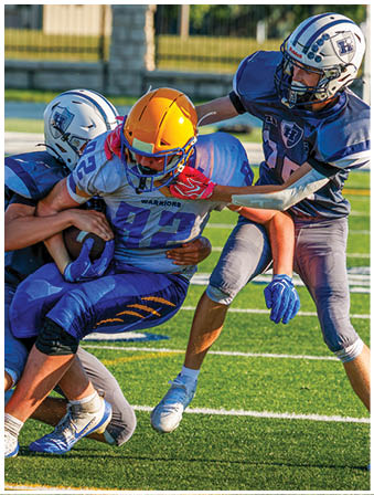Three football players in blue and white uniforms running on a field. Description generated by AI