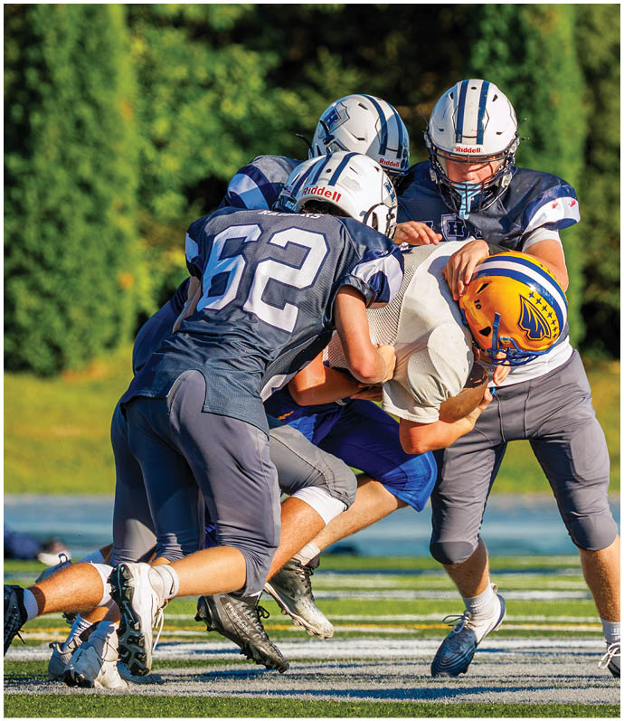 Three football players in blue and white uniforms running on a field. Description generated by AI