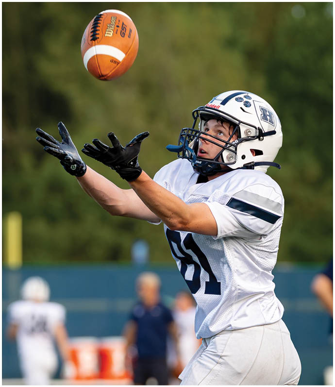 Three football players in blue and white uniforms running on a field. Description generated by AI