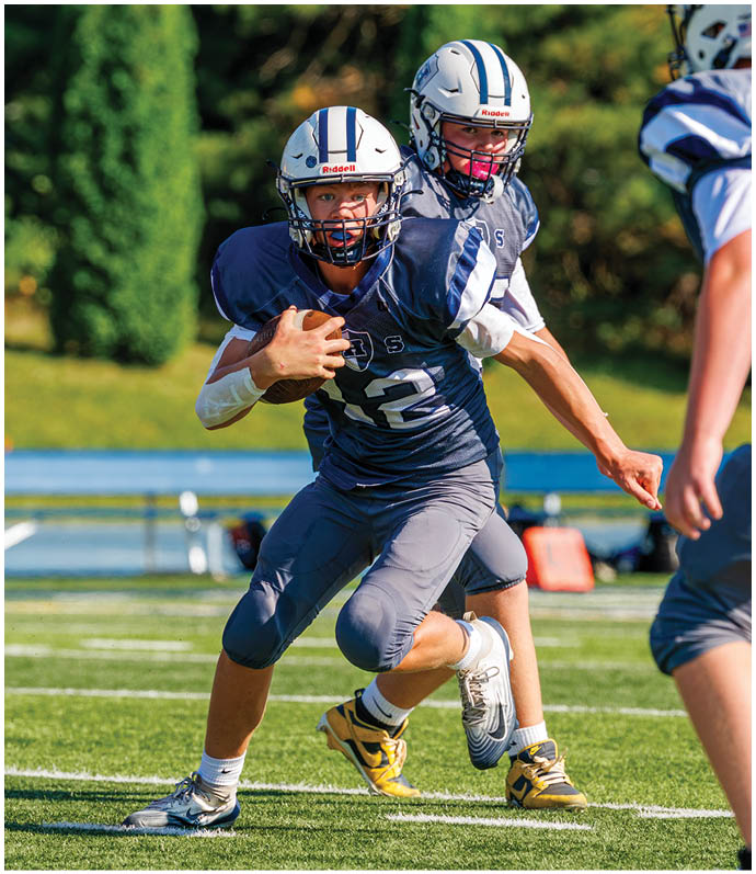 Three football players in blue and white uniforms running on a field. Description generated by AI