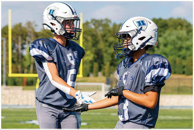 Three football players in blue and white uniforms running on a field. Description generated by AI