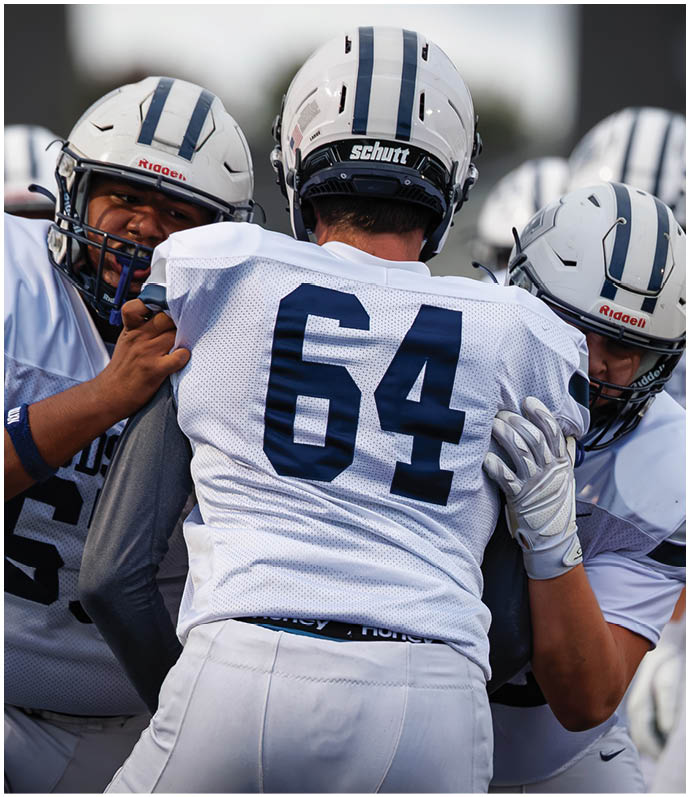 Three football players in blue and white uniforms running on a field. Description generated by AI