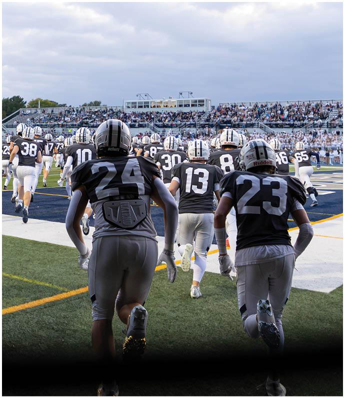 Three football players in blue and white uniforms running on a field. Description generated by AI