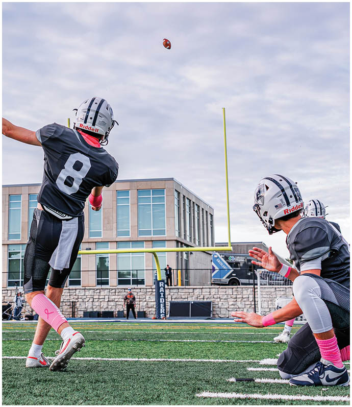 Three football players in blue and white uniforms running on a field. Description generated by AI