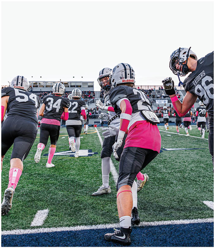 Three football players in blue and white uniforms running on a field. Description generated by AI