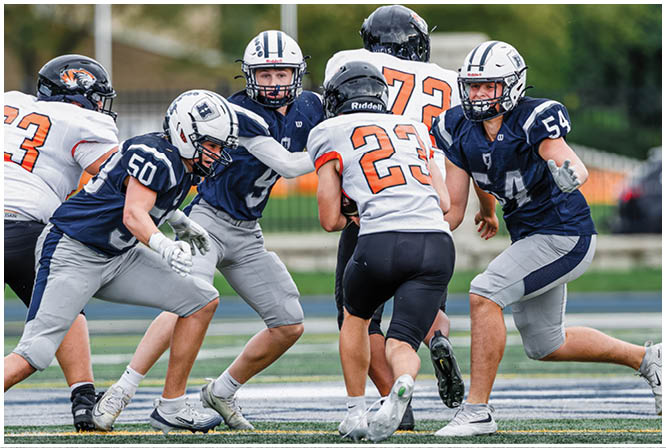 Three football players in blue and white uniforms running on a field. Description generated by AI