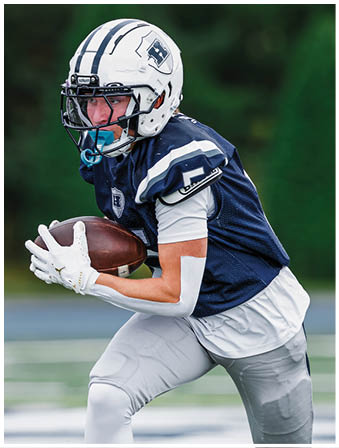 Three football players in blue and white uniforms running on a field. Description generated by AI