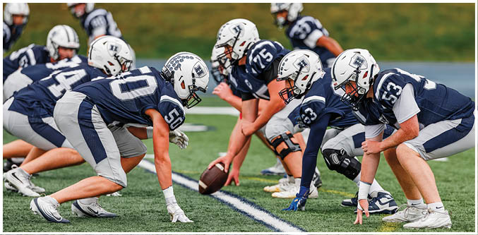 Three football players in blue and white uniforms running on a field. Description generated by AI