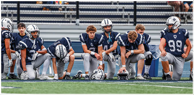 Three football players in blue and white uniforms running on a field. Description generated by AI