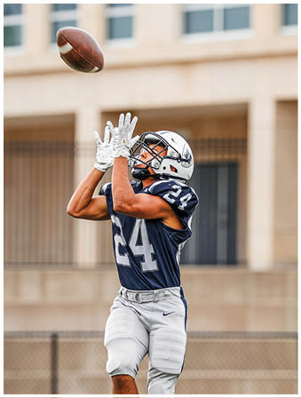 Three football players in blue and white uniforms running on a field. Description generated by AI