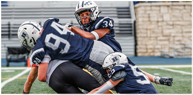 Three football players in blue and white uniforms running on a field. Description generated by AI
