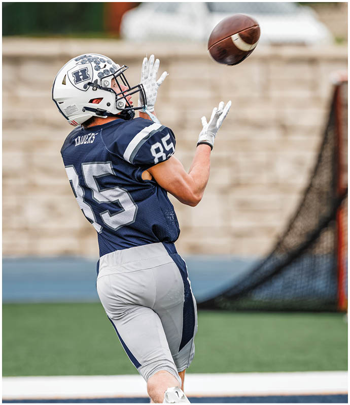 Three football players in blue and white uniforms running on a field. Description generated by AI