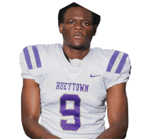 A person wearing a white football jersey with purple stripes and the word “HUEYTOWN" along with the number 9 is kneeling with hands clasped. Description generated by AI