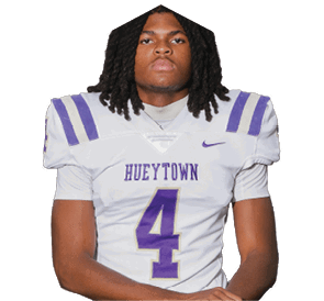 A person with long dreadlocks wearing a white and purple football uniform with the number 4 and the word Hueytown on the jersey is standing with arms crossed. Description generated by AI
