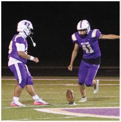 People in football uniforms are actively engaged in a play on a field with one person holding the ball and others positioned for blocking or defense. Description generated by AI