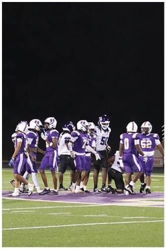 A person wearing a Wildcats football uniform is running on a field while holding a football during a game. Description generated by AI