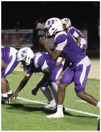 A person wearing a Wildcats football uniform is running on a field while holding a football. Description generated by AI