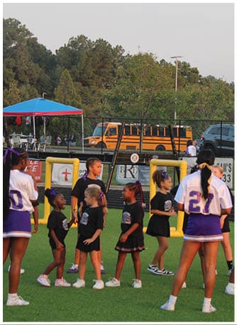 A person wearing a Wildcats football uniform is running on a field while holding a football during a game. Description generated by AI