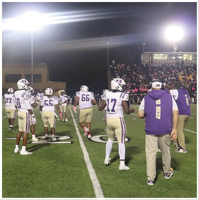 People in football uniforms are actively engaged in a play on a field with one person holding the ball and others positioned for blocking or defense. Description generated by AI