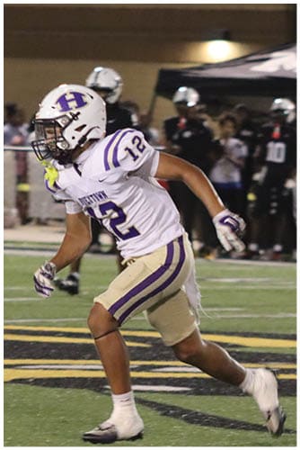 A person wearing a Wildcats football uniform is running on a field while holding a football during a game. Description generated by AI