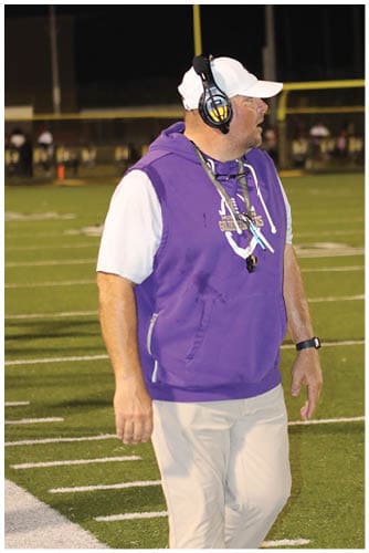 A person wearing a Wildcats football uniform is running on a field while holding a football during a game. Description generated by AI