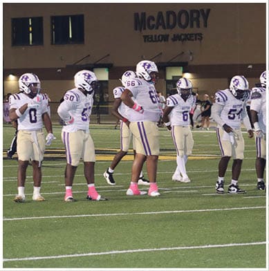People in football uniforms are actively engaged in a play on a field with one person holding the ball and others positioned for blocking or defense. Description generated by AI