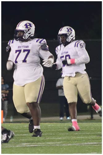 A person wearing a Wildcats football uniform is running on a field while holding a football during a game. Description generated by AI