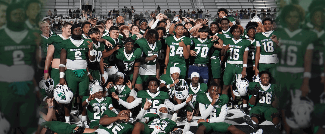 Four people wearing black sports jerseys with “VISTA" on them stand closely together in front of a large crowd, with one person raising an arm in celebration. Description generated by AI