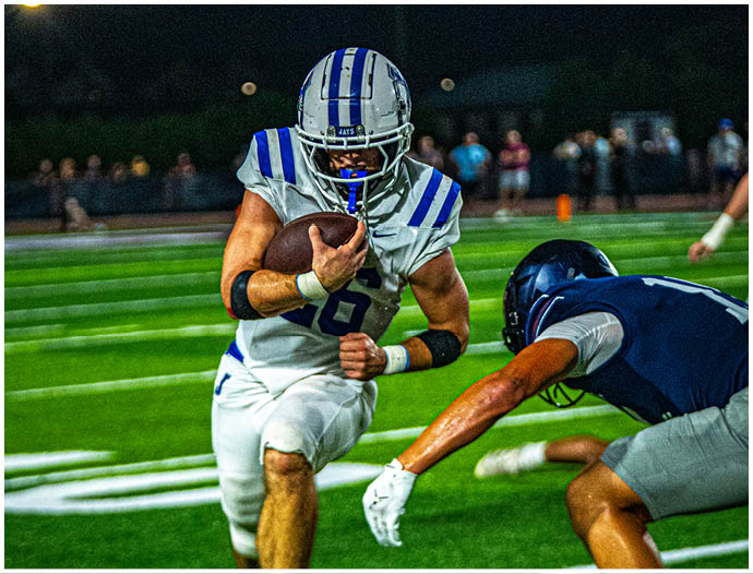 Three football players in blue and white uniforms running on a field. Description generated by AI