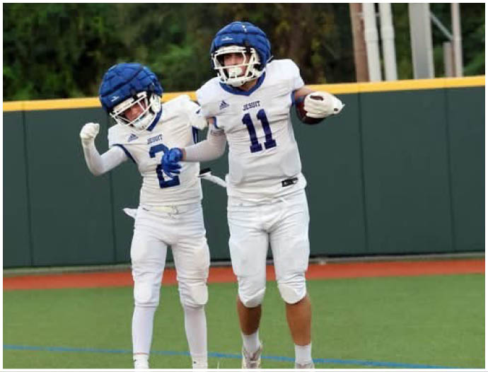 Three football players in blue and white uniforms running on a field. Description generated by AI