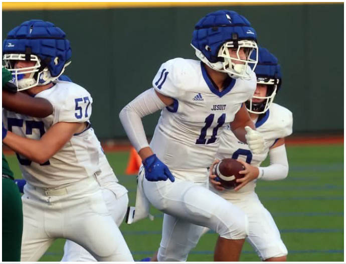 Three football players in blue and white uniforms running on a field. Description generated by AI
