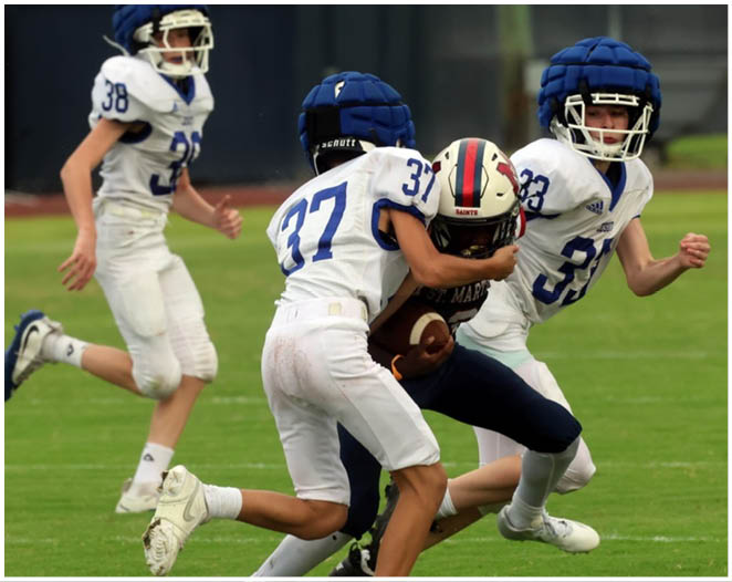 Three football players in blue and white uniforms running on a field. Description generated by AI