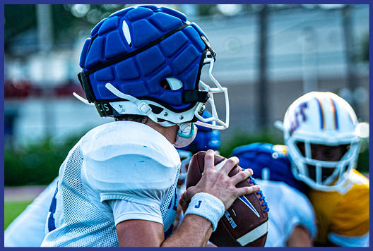 Three football players in blue and white uniforms running on a field. Description generated by AI