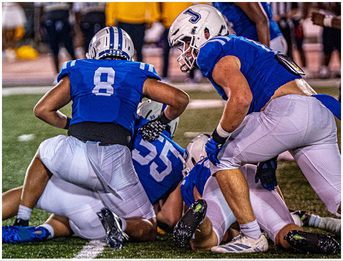Three football players in blue and white uniforms running on a field. Description generated by AI