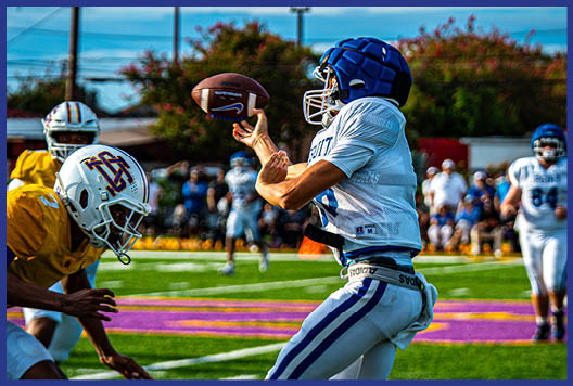 Three football players in blue and white uniforms running on a field. Description generated by AI